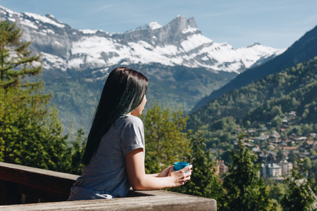 girl holding cup while standing on balcony and looking at scenic mountains, mont blanc, alpsの写真素材
