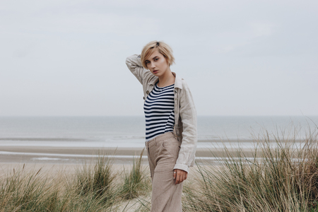 stylish young woman in striped shirt and jacket on sandy shoreの写真素材