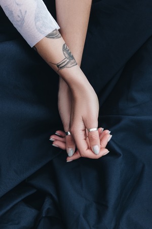 cropped view of tattooed girl hands with rings on black cloth