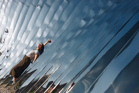 WROCLAW, POLAND - 18 MAY 2018: relaxed young woman in front of sculpture made of reflective materialの写真素材
