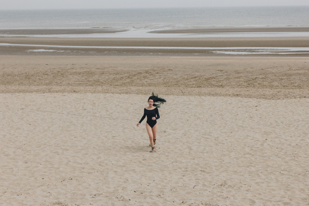 attractive young woman in black bodysuit running on sandy seashoreの写真素材