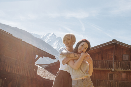 beautiful happy girls hugging while standing between wooden houses in mountain village, mont blanc, alpsの写真素材