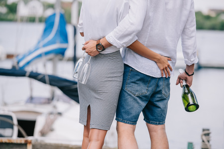 cropped shot of young couple holding wine glasses and bottle, hugging at seasideの写真素材