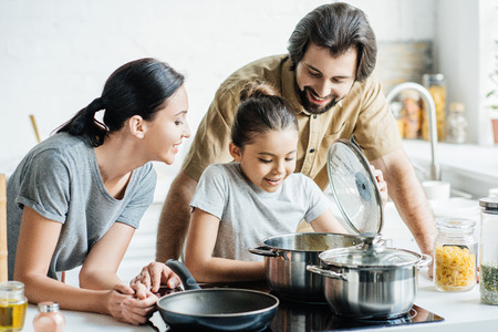 smiling young family cooking together at kitchenの写真素材