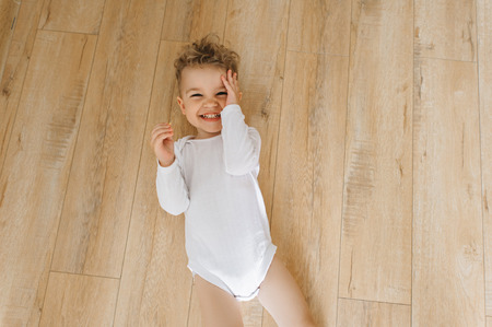 overhead view of cute little smiling boy in white bodysuit lying on floor at homeの写真素材