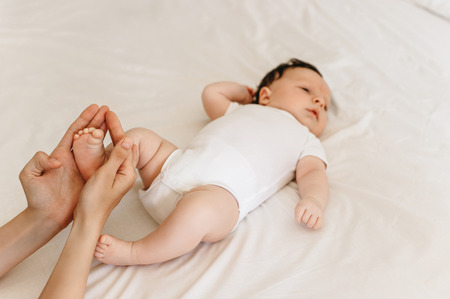cropped shot of mother holding foot of little infant baby on bed at homeの写真素材