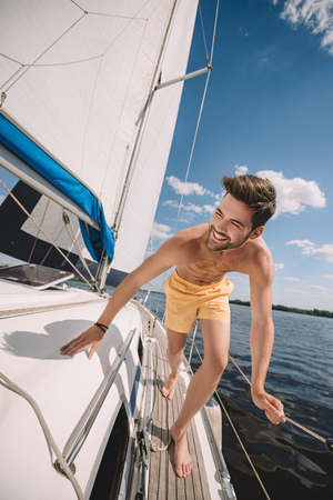 smiling shirtless man in swim trunks running on yachtの写真素材