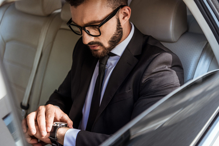 handsome businessman in suit checking time on wristwatch in carの写真素材
