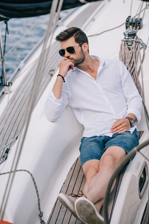 high angle view of pensive young man in sunglasses looking away while sitting on yachtの写真素材