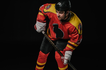 professional hockey player in protective sportswear holding hockey stick and looking away isolated on blackの写真素材