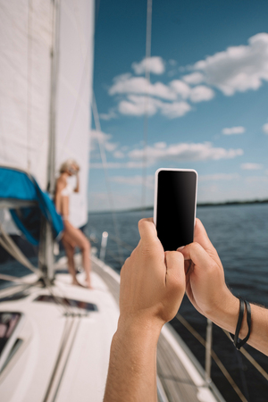 cropped image of man taking picture of girlfriend on smartphone on yachtの写真素材