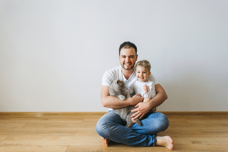 smiling father holding little son in bodysuit and grey british shorthair cat in hands at homeの写真素材