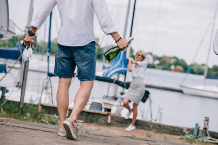 cropped shot of man holding wine glasses and bottle while happy girl standing near yachtの写真素材