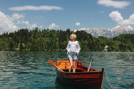beautiful young woman in sunglasses standing in boat at tranquil mountain lake, bled, sloveniaの写真素材