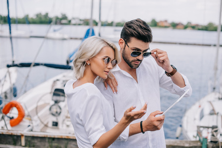 beautiful stylish young couple in sunglasses using digital tablet on yachtの写真素材
