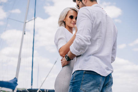 low angle view of beautiful stylish young couple in sunglasses hugging on yachtの写真素材