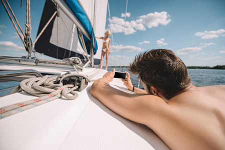 selective focus of man taking picture of girlfriend on smartphone on yacht