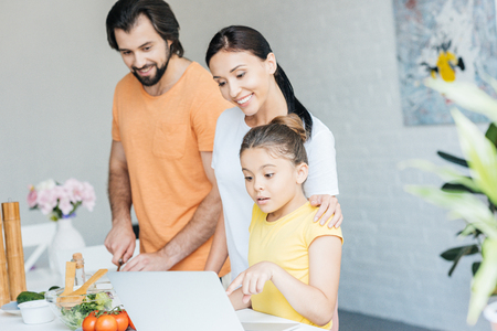 smiling young family using laptop together at kitchenの写真素材