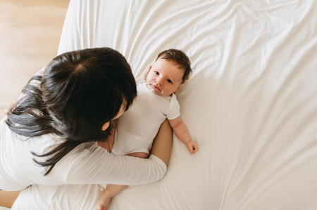 overhead view of mother putting little infant baby on bed at homeの写真素材