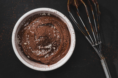 top view of bowl with chocolate pudding and whisk on black table