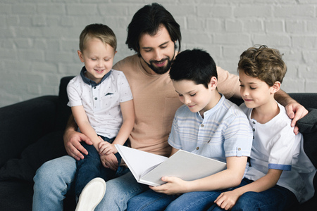 portrait of father and sons reading book together at home
