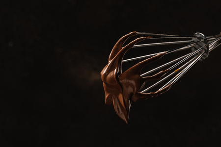 yummy chocolate on whisk isolated on blackの写真素材
