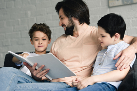 portrait of smiling father and sons reading book together at homeの写真素材