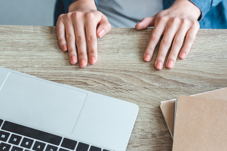 close-up partial view of female hands on wooden table with laptop and notebooksの写真素材