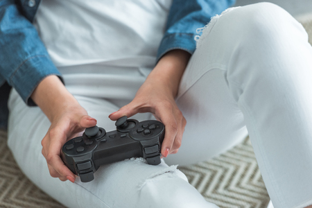 close-up partial view of girl playing with joystick while sitting on carpet