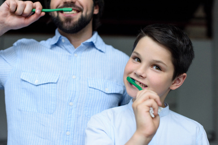 partial view of father and son brushing teeth together at home