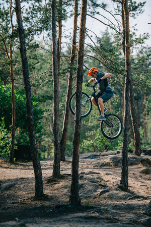 young trial biker jumping on bicycle at pine forestの写真素材