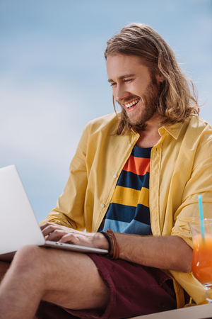 smiling young man using laptop at summer dayの写真素材