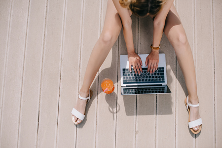 cropped shot of pretty girl using laptop while sitting on wooden surface at sunny dayの写真素材