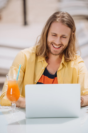 smiling young man using laptop while sitting outdoors at sunny dayの写真素材