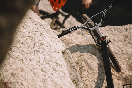selective focus of mountain bike on rock and male extreme cyclist in helmet riding on bicycle behindの写真素材