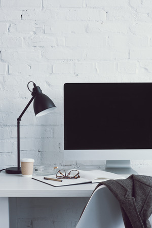 computer and disposable coffee cup on table in modern workspaceの写真素材