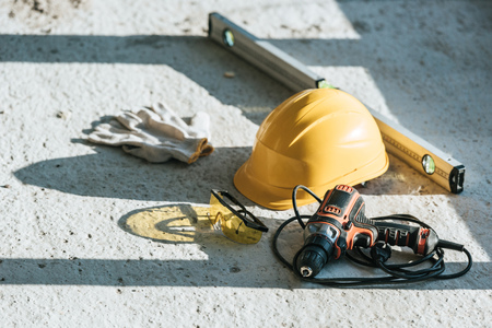 close up view of hardhat, spirit level, drill and protective gloves with goggles at construction...