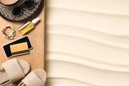 flat lay with straw hat, flip flops, smartphone and credit car don wooden plank on sandy beachの写真素材