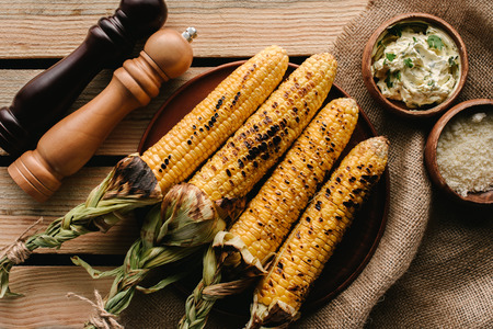 top view of grilled corn, salt and pepper grinders on wooden table with sackclothの写真素材
