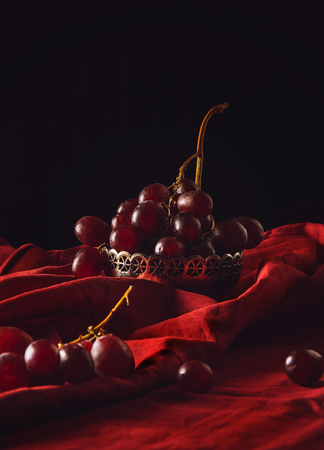 close-up shot of ripe grapes in vintage metal bowl on red drapery on blackの写真素材