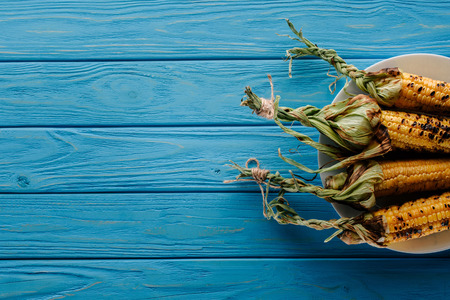 top view of grilled corn on plate on blue wooden table