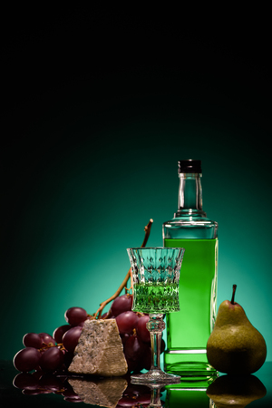 close-up shot of absinthe with fresh pear, grapes and cheese on mirror surface on dark blue backgroundの写真素材