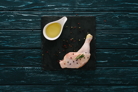 top view of chicken leg with pepper corns and oil on stone boardの写真素材