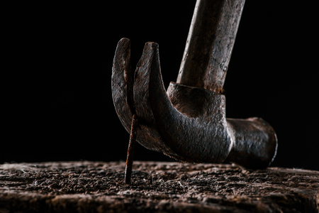 close up view of vintage rusty hammer and nail in wooden stump isolated on blackの写真素材