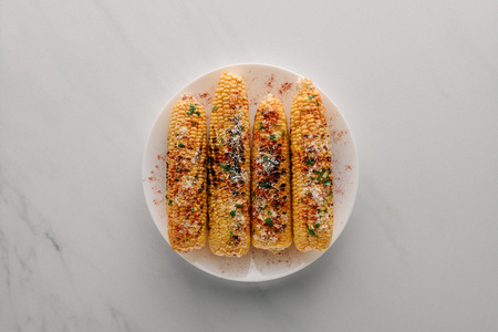 top view of grilled corn with salt and chili spice on plate on marble tableの写真素材