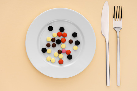 top view of fork, knife and plate with various pills on beige background