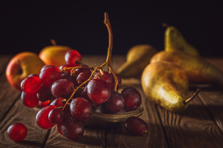 close-up shot of ripe pears and grapes on rustic wooden table on blackの写真素材