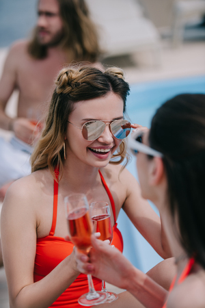 selective focus of young female friends drinking champagne and smiling at poolの写真素材