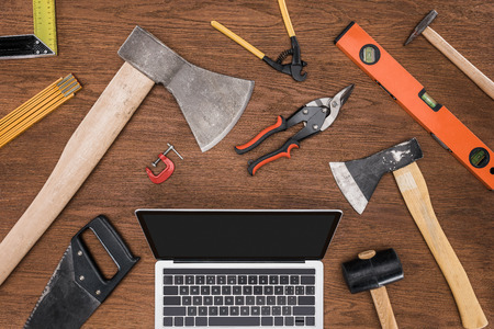 top view of laptop with blank screen surrounded by various tools on wooden tableの写真素材