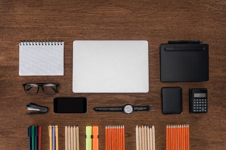 top view of workplace with arranged pencils, empty textbook, smartphone and laptop on wooden tableの写真素材